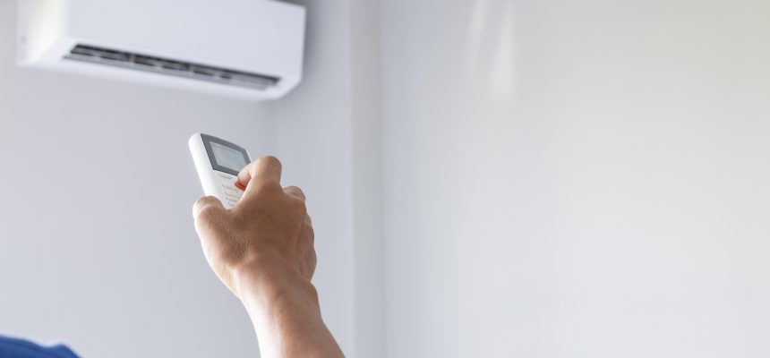 Close-up Of Man Hand Operating Air Conditioner With Remote Control.