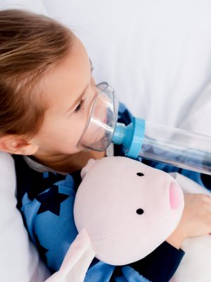 sick kid using inhaler with spacer and holding soft toy