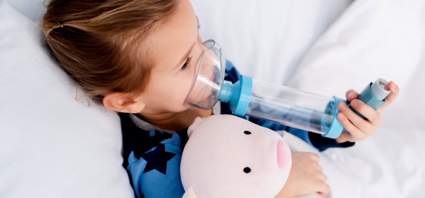 sick kid using inhaler with spacer and holding soft toy